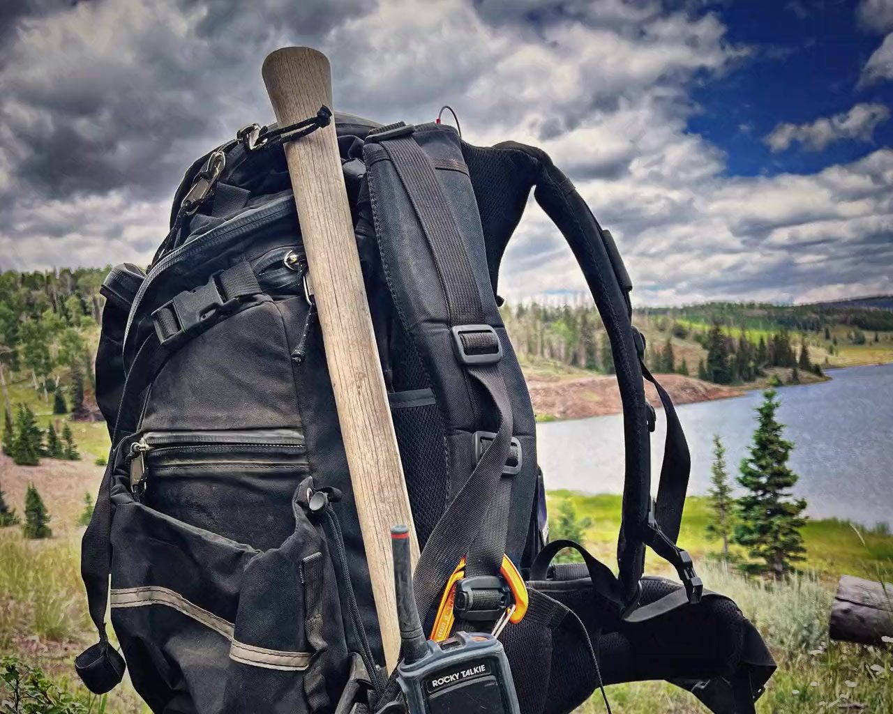 A line pack with a tool handle and a radio, set down above a mountain lake