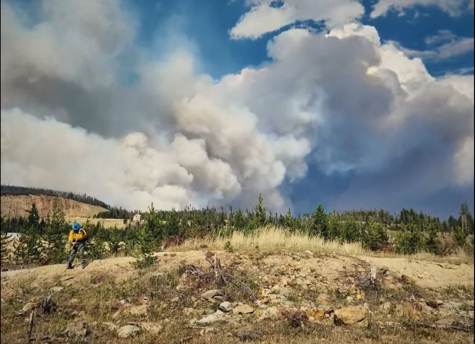 A lone firefighter on a hillside below a huge smoke column