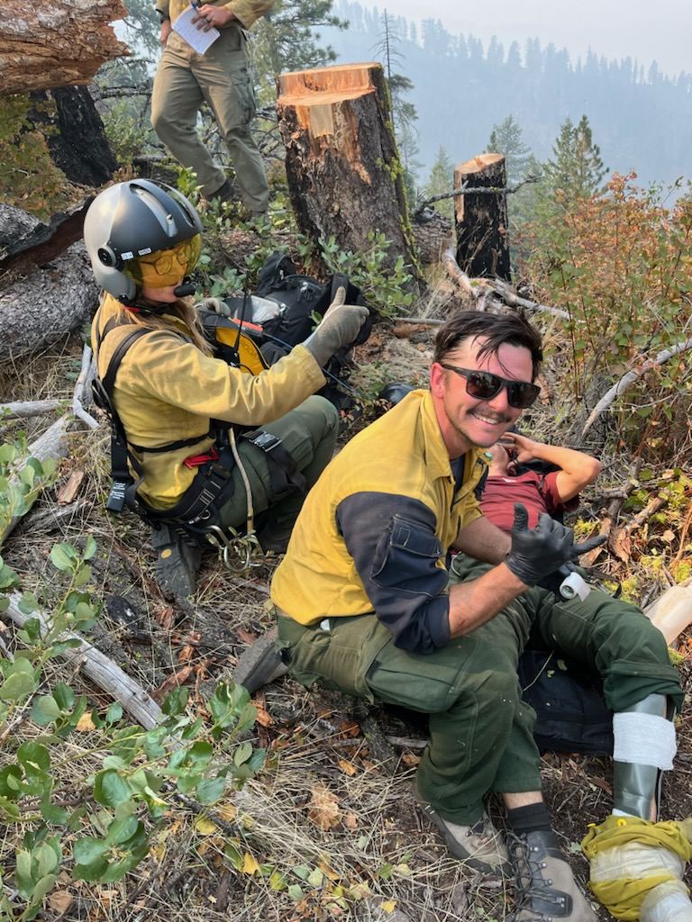 Two firefighters on the line giving a thumbs up beside a patient with a splinted leg