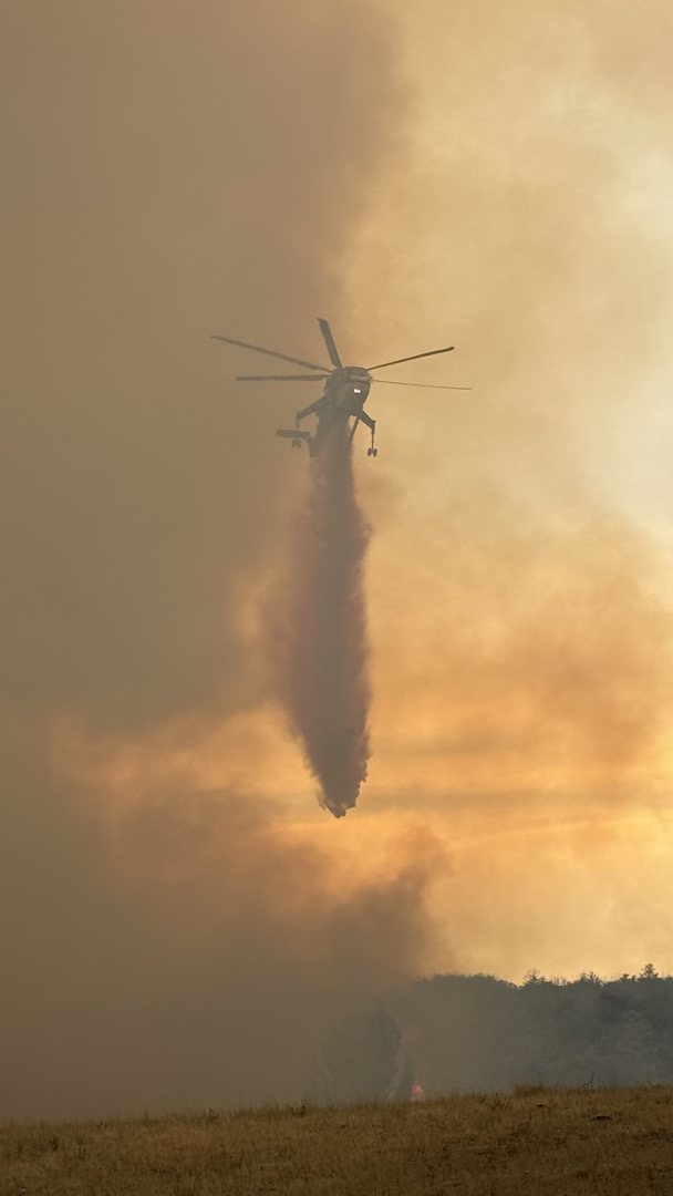 A helicopter making a bucket drop into smoke at sunset