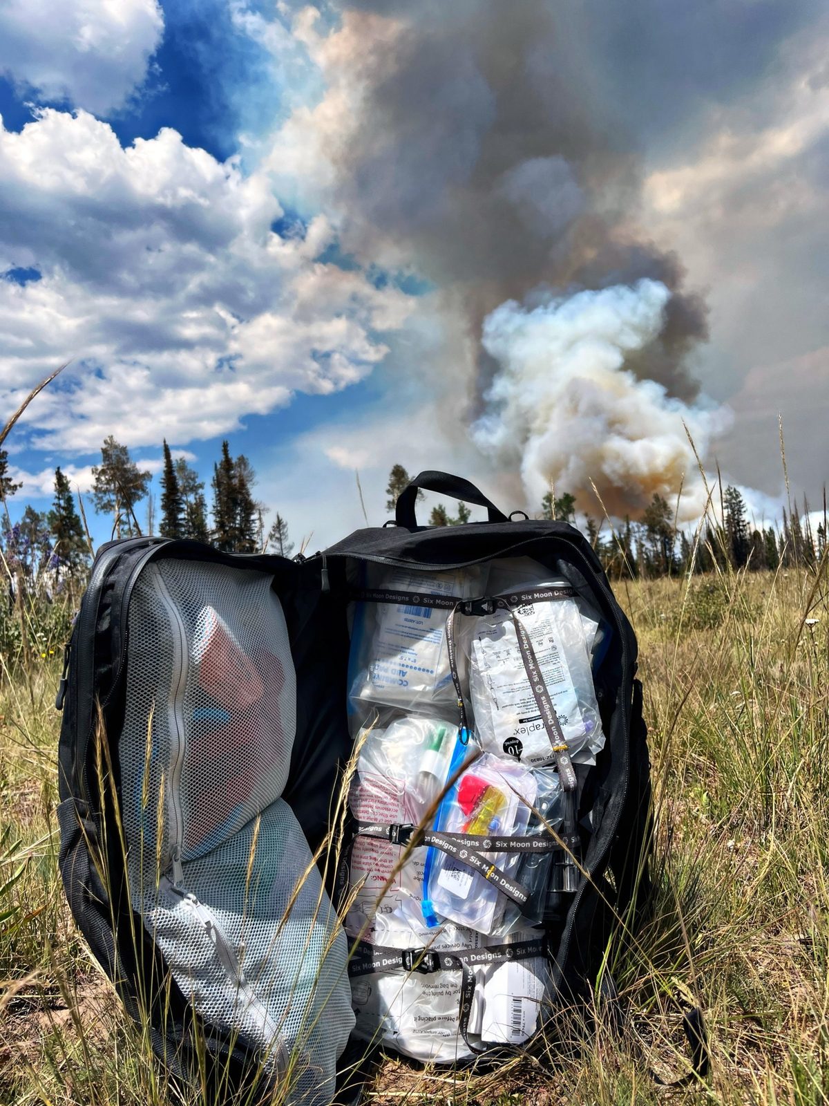 An open EMS bag on the grass with a smoke column behind it